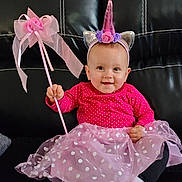 Ophélya participe au concours pour gagner de l'argent avec cette photo : baby, child, unicorn_costume, headband, tutu, pink, polka_dots, wand, smiling, sitting, leather_couch, indoor, cute, happy, costume, dress, footwear, black_background, portrait, person
