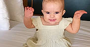 Lilia is registered to the contest to win money with this photo: baby, child, infant, bed, dress, smiling, arms_up, anchor, wall_decor, rope, white_bedspread, pillow, indoor, person, cute, furniture, room, happy, sitting, portrait
