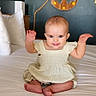 baby, child, infant, bed, dress, smiling, arms_up, anchor, wall_decor, rope, white_bedspread, pillow, indoor, person, cute, furniture, room, happy, sitting, portrait