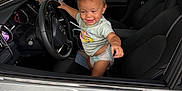 Aizen joined the competition — help win amazing prizes! toddler, child, car, steering_wheel, diaper, tshirt, smiling, inside_car, driver_seat, pointing, silver_car, happy, young_child, automobile_interior, seat, window, door_handle, outdoor, greenery, playful