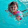 child, swimming_pool, water, floaties, watermelon_pattern, smiling, wet_hair, summer, playful, gesture, recreation, outdoor_activity, kid, fun, happy, splash, blue, cute, person, leisure