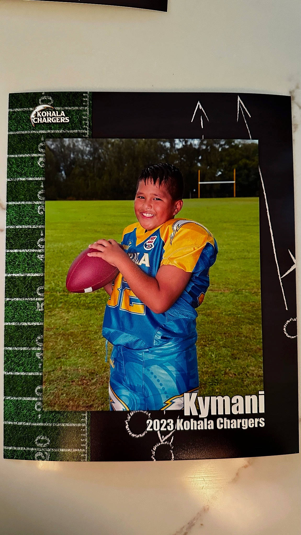 Kymani is registered to the contest to win money with this photo: advertising, denim, electric_blue, font, graphic_design, grass, happy, jersey, joy, logo, pattern, person, photo_caption, player, rectangle, sleeve, smile, sports_collectible, sportswear, t_shirt
