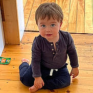 Henri is registered to the contest to win money with this photo: child, toddler, baby, portrait, sitting, barefoot, smiling, blue_eyes, brown_hair, dark_clothing, wooden_floor, indoor, home, floorboards, snack_package, candid, adorable, looking_at_camera, natural_light, photography