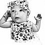 baby, infant, headband, bow, cartoon_print, black_and_white, portrait, cute, clothing, patterned, arms, face, eyes, curious, smile, child, young, studio, closeup, soft_focus