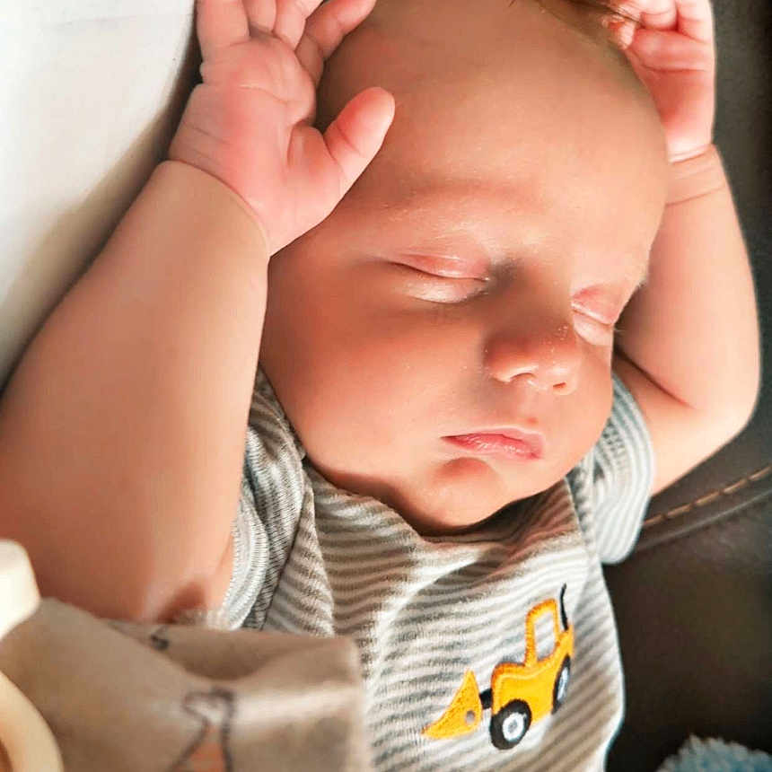 Soryn is registered to the contest to win money with this photo: arms_up, baby, blanket, casual_clothing, child, construction_vehicle, couch, cute, face, indoors, infant, newborn, peaceful, portrait, relaxation, resting, sleeping, soft_texture, striped_shirt, young_child