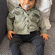 Lyzio participe au concours pour gagner de l'argent avec cette photo : baby, bear_design, black_socks, child, clothing, couch, cushion, cute, denim_jacket, hair_styled, home, indoor, pacifier, patterned_rug, relaxed, seated, smiling, socks, toddler, white_socks