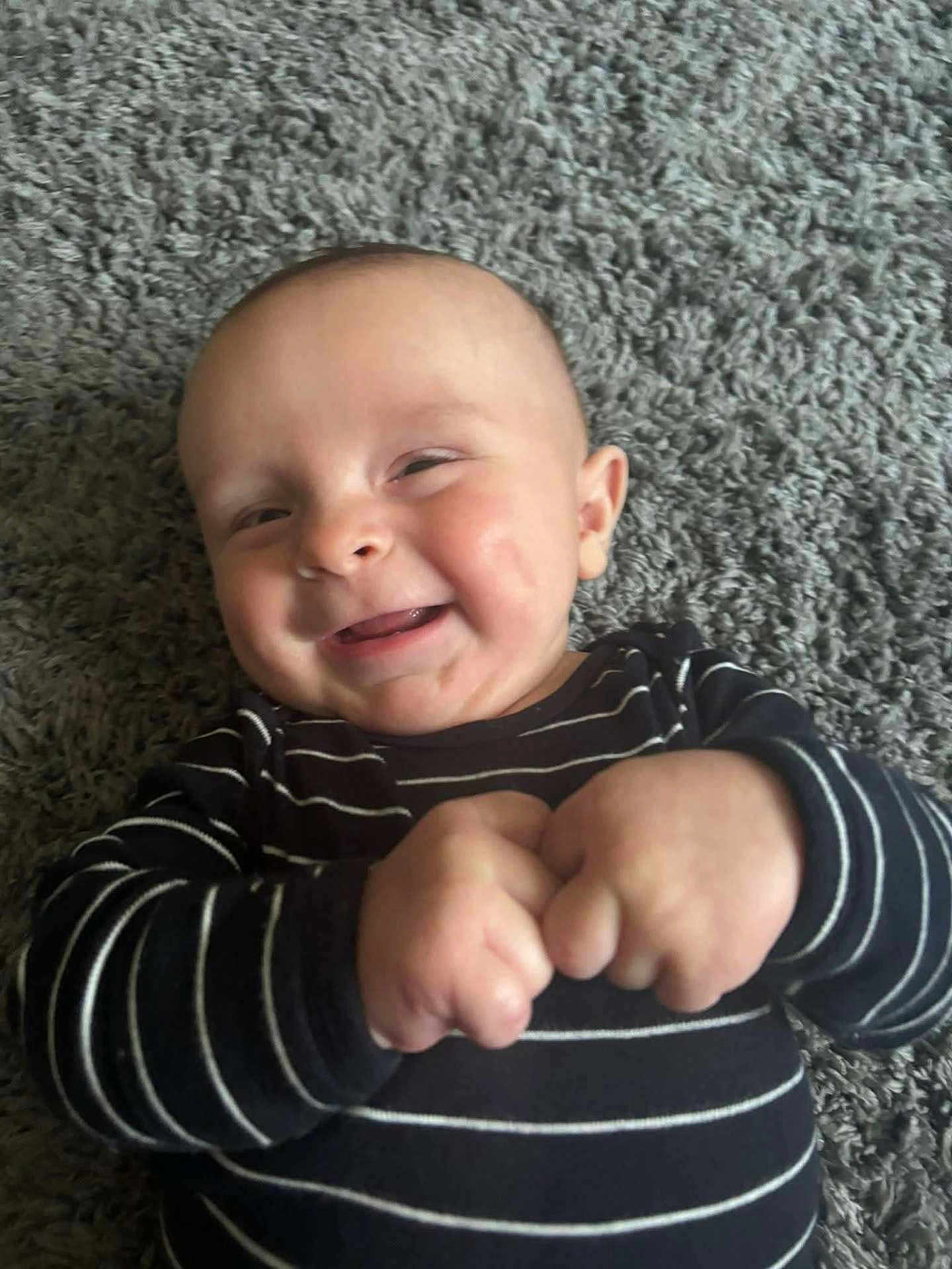 Wyatt is registered to the contest to win money with this photo: baby, infant, smiling, hands, carpet, striped_clothing, happy, cute, child, portrait, indoor, closeup, person, young, skin, head, face, expression, fingers, toddler
