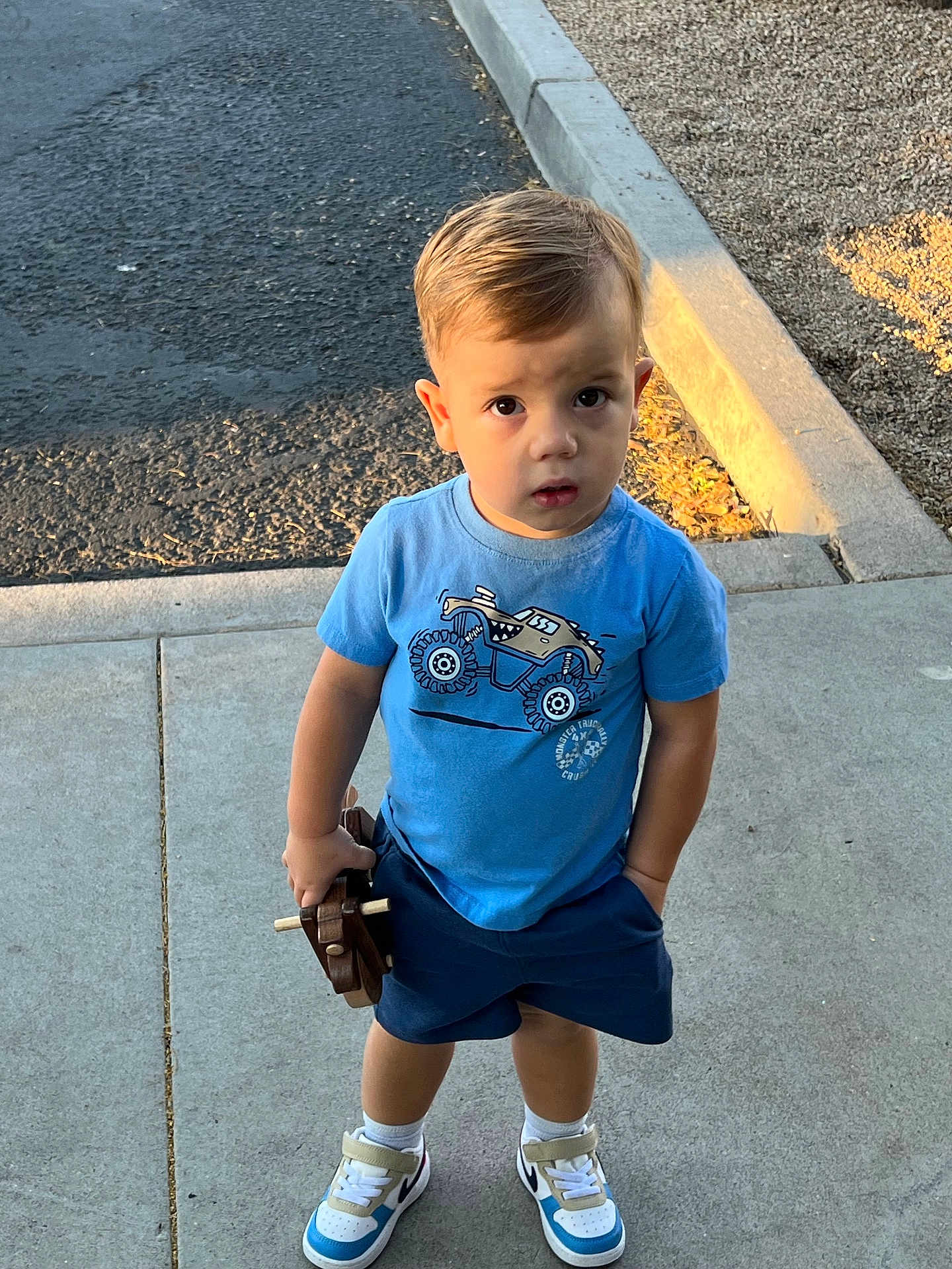 Adam joined the competition — help win amazing prizes! toddler, child, sidewalk, toy, wooden_toy, blue_tshirt, shorts, sneakers, outdoor, curious, sunlight, concrete, casual_clothing, young_child, standing, playtime, daylight, expression, park, summer