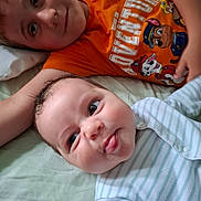 James joined the competition — help win amazing prizes! baby, bed, boy, cartoon_characters, child, cute, face, happy, indoor, infant, lying_down, orange_shirt, pajamas, portrait, shirt, siblings, smiling, striped_onesie, toddler, tongue_out