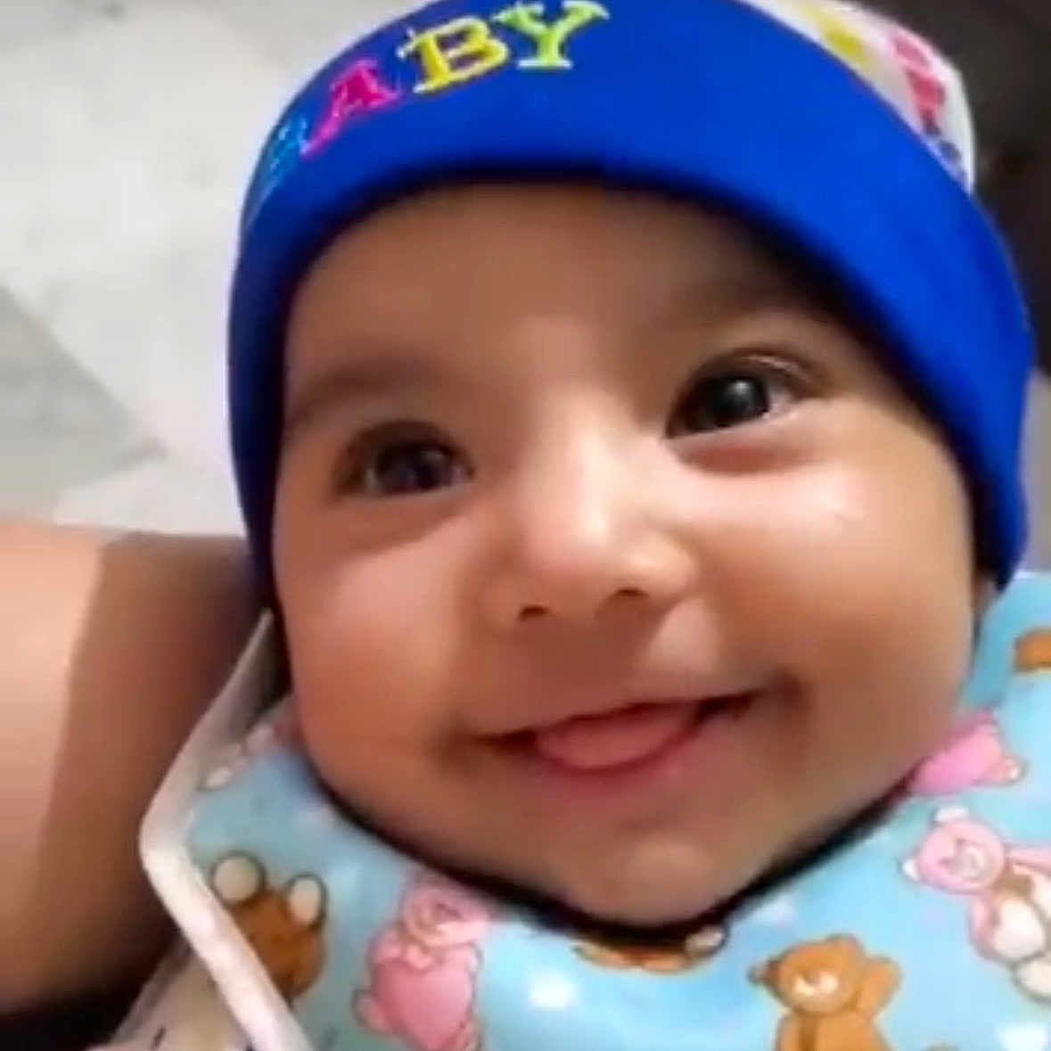 Aditi Joshi is registered to the contest to win money with this photo: baby, smiling, blue_hat, bib, teddy_bear_pattern, cute, infant, child, face, happy, tongue_out, closeup, apparel, headwear, indoors, person, portrait, young_child, adorable, bright_eyes
