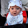 baby, infant, hat, bib, blanket, clothing, face, wide_eyes, expression, cute, teddy_bear_pattern, newborn, portrait, child, sitting, cozy, soft_texture, red_strap, mouth_open, cute_expression
