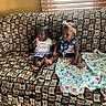 baby, babies, child, children, couch, sofa, blanket, headband, patterned_fabric, indoors, window_blinds, carpet, foot, sitting, curious, clothing, person, two_people, home_interior, cute