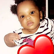 Nevaeh is registered to the contest to win money with this photo: baby, child, face, curly_hair, striped_shirt, heart_emoji, phone_screen, portrait, cute, infant, expression, black_background, mobile_phone, small_ponytails, looking_at_camera, indoors, close_up, person, digital_photo, emoji
