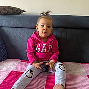 Milena is registered to the contest to win money with this photo: toddler, child, pink_hoodie, penguin_pants, sitting, blanket, computer_mouse, indoor, couch, cushion, curly_hair, small_pony_tail, blue_eyes, socks, casual_clothing, cute, portrait, person, home_interior, innocence