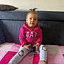 toddler, child, pink_hoodie, penguin_pants, sitting, blanket, computer_mouse, indoor, couch, cushion, curly_hair, small_pony_tail, blue_eyes, socks, casual_clothing, cute, portrait, person, home_interior, innocence