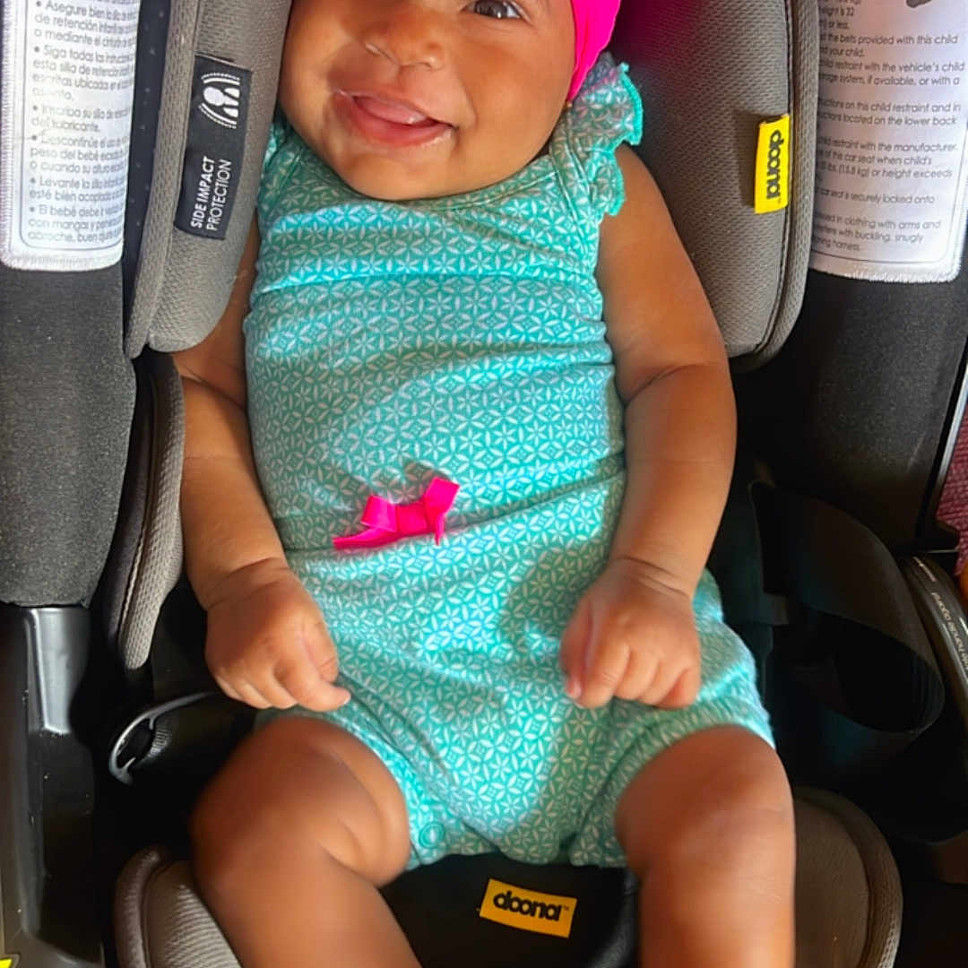 Zoe is registered to the contest to win money with this photo: baby, bonnet, cap, car, car_interior, carseat, clothing, cushion, dress, face, happy, hat, head, homedecor, person, photography, portrait, smile, transportation, vehicle