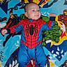 baby, child, spiderman_costume, superhero, marvel, blanket, colorful, infant, lying_down, cute, smiling, fist, cape, comic_characters, blue, red, green, yellow, portrait, indoor