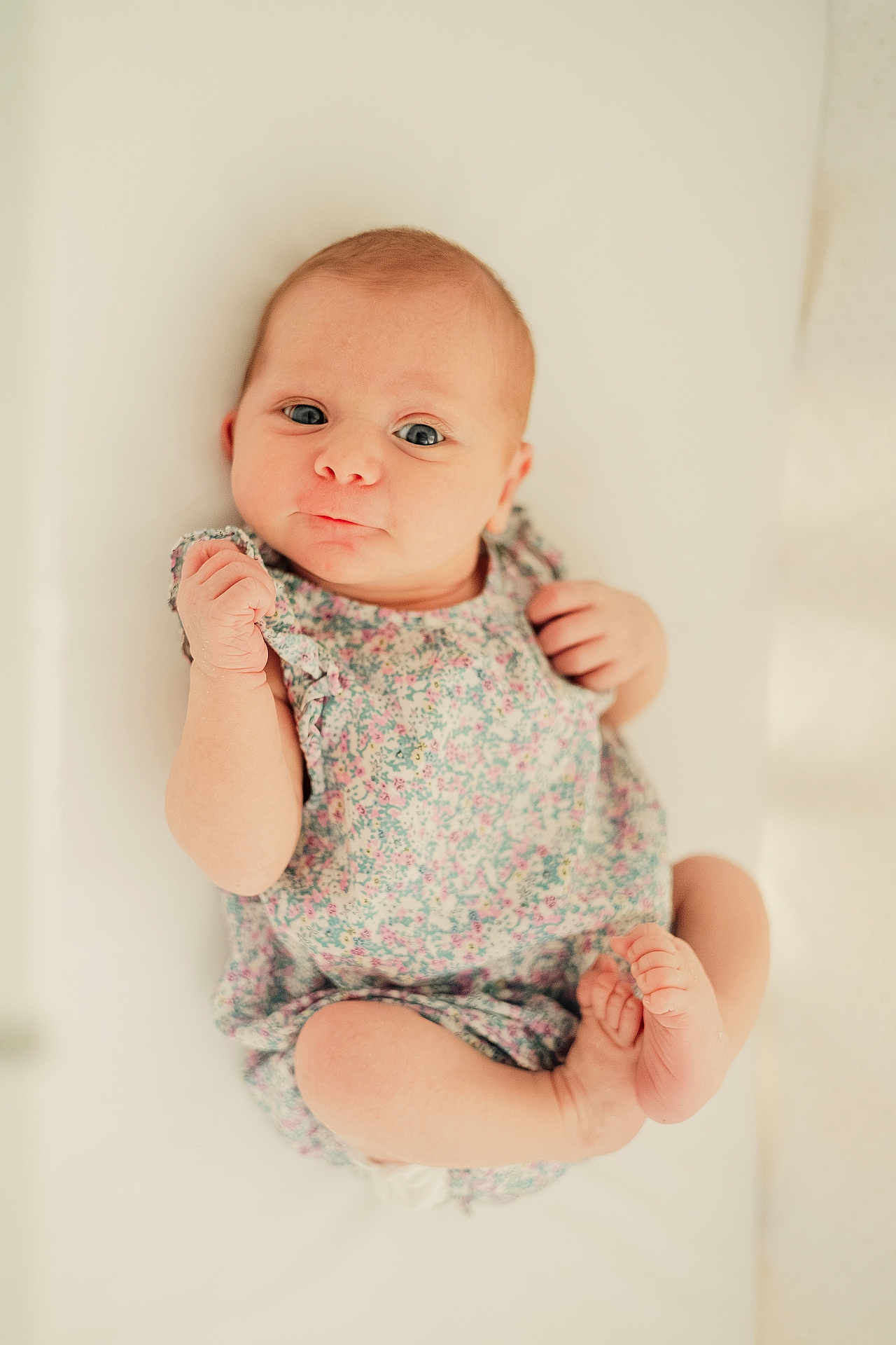 Maddy participe au concours pour gagner de l'argent avec cette photo : baby, infant, child, floral_dress, cute, lying_down, soft_light, white_background, skin, face, hands, feet, expression, portrait, newborn, young_child, human, apparel, closeup, peaceful