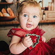 Elodie joined the competition — help win amazing prizes! baby, child, blue_eyes, red_dress, cookie_cutter, kitchen, indoor, portrait, cute, toddler, curly_hair, holding, expression, face, person, smile, furniture, background, window, sitting