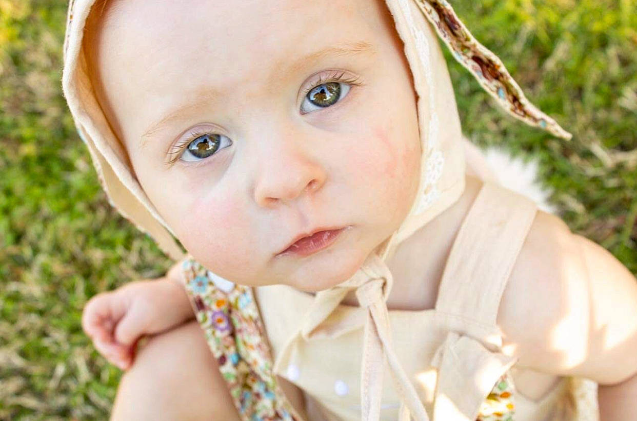 Blakely is registered to the contest to win money with this photo: baby, baby_toddler_clothing, cheek, dress, eye, eyelash, finger, fun, grass, hand, happy, headwear, iris, leaf, lip, nose, people_in_nature, person, plant, skin