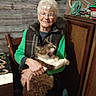 cabinet, cat, chair, cozy, decor, domestic, elderly_woman, fan, furniture, glasses, green_sleeves, hand, happy, indoor, pet, plaid_vest, smile, table, wooden_wall, yawning_cat
