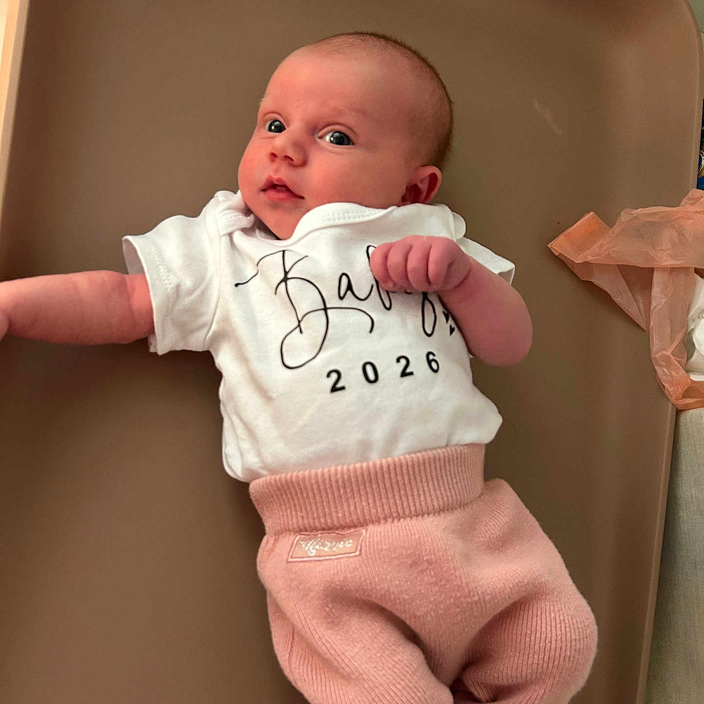 Théa participe au concours pour gagner de l'argent avec cette photo : baby, infant, clothing, white_shirt, pink_pants, lying_down, face, eyes, newborn, cute, changing_pad, indoors, soft_texture, skin, person, child, apparel, looking, baby_gear, curious