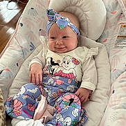Maycee May Jones is registered to the contest to win money with this photo: baby, infant, smiling, headband, clothing, pants, socks, baby_seat, floral_pattern, indoor, blanket, couch, wood_floor, cute, comfort, person, face, hand, footwear, head