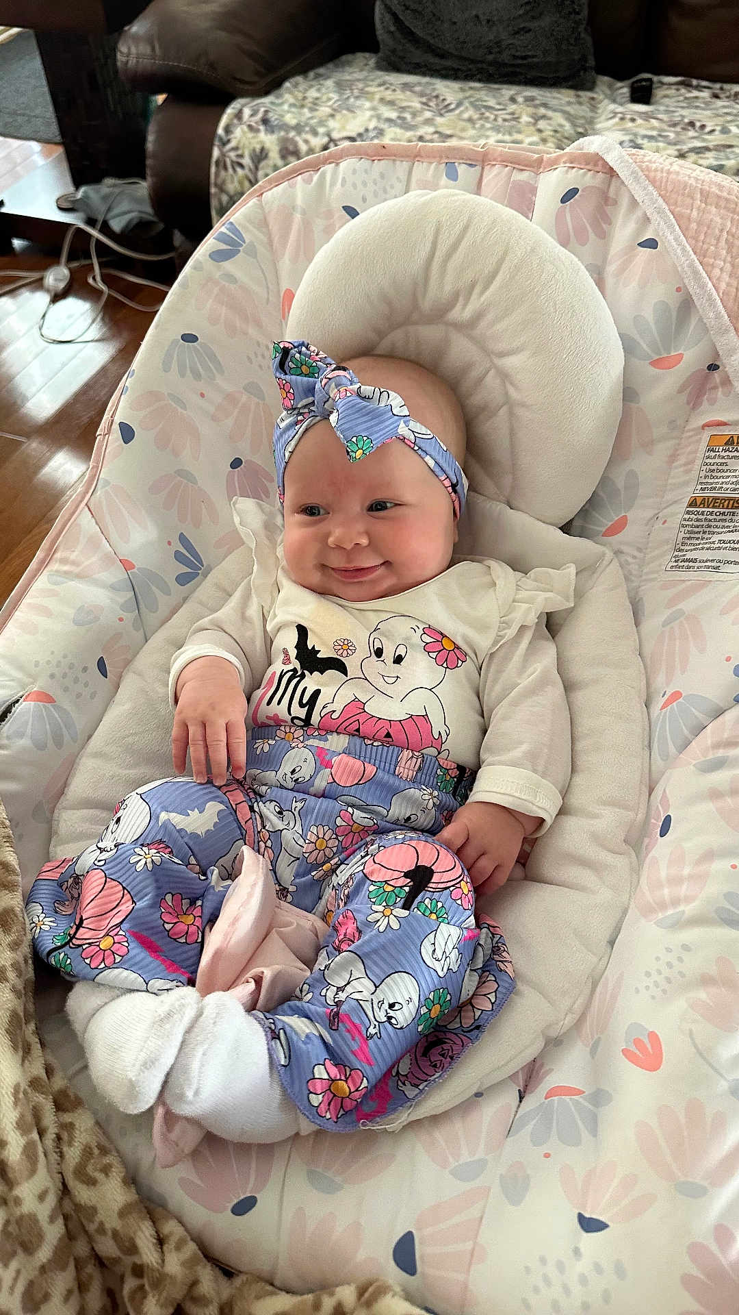 Maycee May Jones is registered to the contest to win money with this photo: baby, infant, smiling, headband, clothing, pants, socks, baby_seat, floral_pattern, indoor, blanket, couch, wood_floor, cute, comfort, person, face, hand, footwear, head