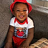 Jarriett joined the competition — help win amazing prizes! baby, child, smiling, red_hat, red_shorts, white_shirt, cartoon_tshirt, sitting, couch, gray_couch, plush, happy, tongue_out, indoors, cute, portrait, young_child, infant, homedecor, cozy