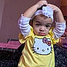 toddler, child, headband, flower, yellow_shirt, hello_kitty, patterned_pants, indoor, serious_expression, person, sitting, clothing, cute, young_child, portrait, baby, face, head, long_sleeve, casual