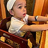 toddler, child, headband, leopard_print, high_chair, bandage, curious, wide_eyes, white_shirt, table, wooden_chair, indoor, earrings, short_sleeves, sneakers, expression, skin, furniture, floor, person