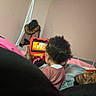 child, adult, tablet, animation, curly_hair, indoor, bed, blanket, coat, relaxed, watching, technology, family, casual, pink, gray, person, furniture, portrait, home
