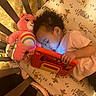 toddler, child, crib, tablet, plush_toy, care_bear, winnie_the_pooh, bed, sleeping, earrings, pink_clothing, patterned_bedding, toy, indoor, cozy, person, cute, curly_hair, resting, technology