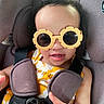 toddler, child, sunglasses, yellow, flower_shaped, car_seat, seatbelt, smile, baby, clothing, straps, cute, happy, indoor, person, eyewear, sitting, hand, closeup, face