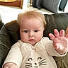 baby, child, onesie, cat_face, couch, leather, curtains, floor, tile, indoor, person, infant, hand, face, clothing, home, reaching, cute, expression, sitting