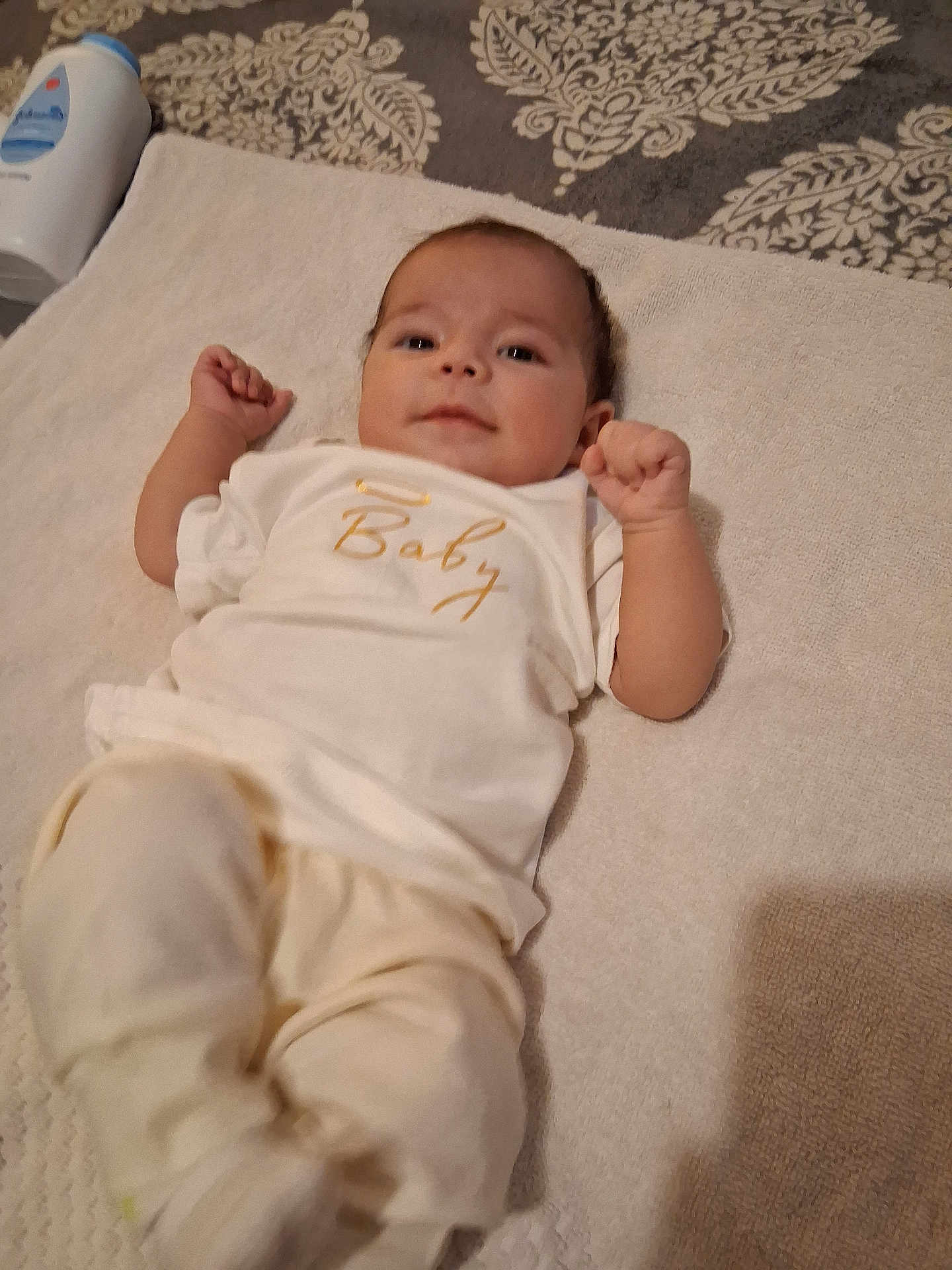 Kali is registered to the contest to win money with this photo: baby, infant, towel, clothing, lying_down, face, smile, hand, arm, leg, bottle, baby_lotion, fabric, pattern, bed, soft, cute, person, indoor, comfort