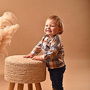 Raphaël participe au concours pour gagner de l'argent avec cette photo : toddler, child, smile, standing, stool, woven_stool, plaid_shirt, jeans, socks, beige_background, studio, happy, cute, indoor, person, furniture, decor, fluffy_plant, portrait, casual_clothing