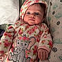 baby, infant, onesie, floral_pattern, elephant_design, pillow, bed, sleepwear, cute, child, portrait, indoor, cozy, soft_fabric, hand, face, head, expression, newborn, blanket