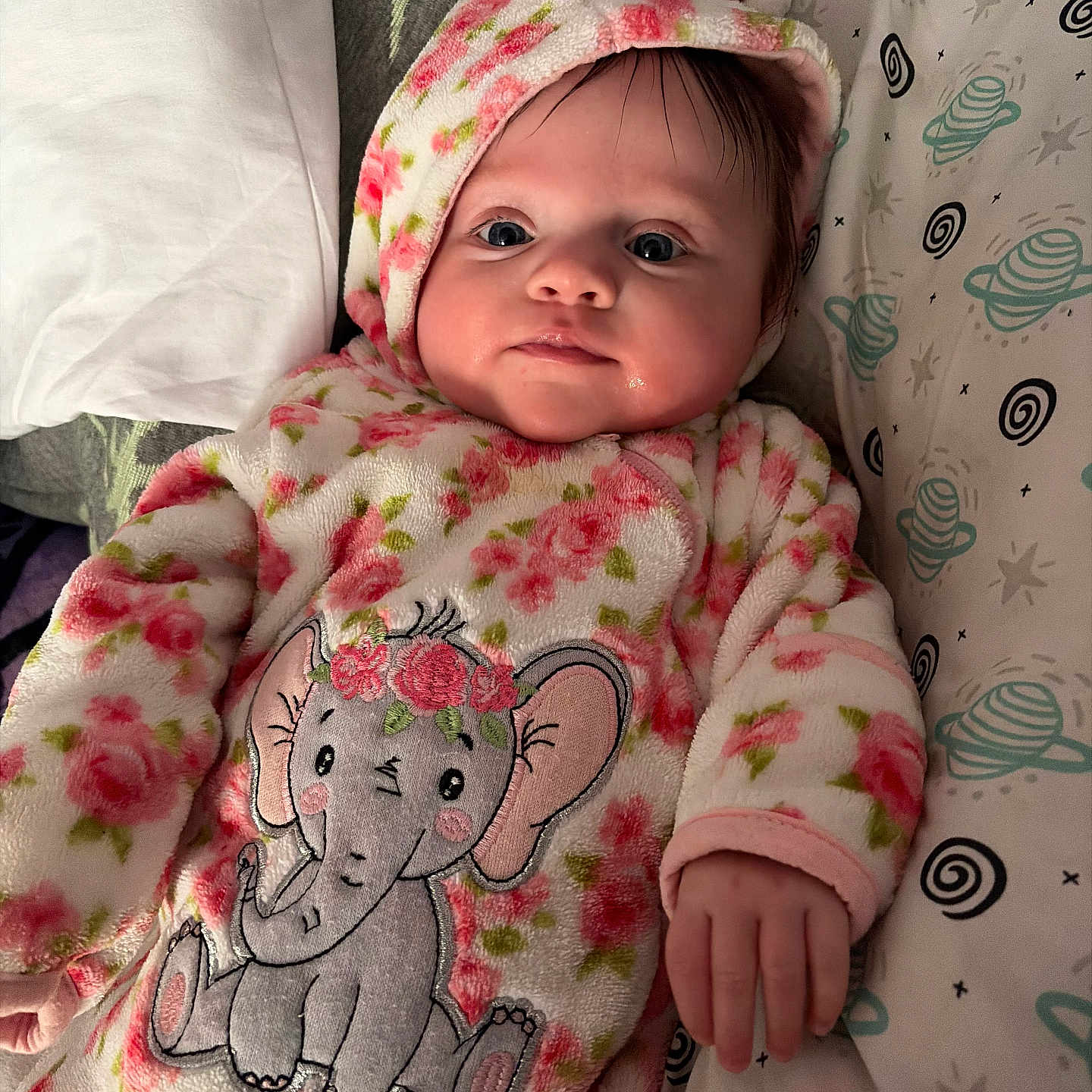 Nora is registered to the contest to win money with this photo: baby, bed, blanket, child, cozy, cute, elephant_design, expression, face, floral_pattern, hand, head, indoor, infant, newborn, onesie, pillow, portrait, sleepwear, soft_fabric