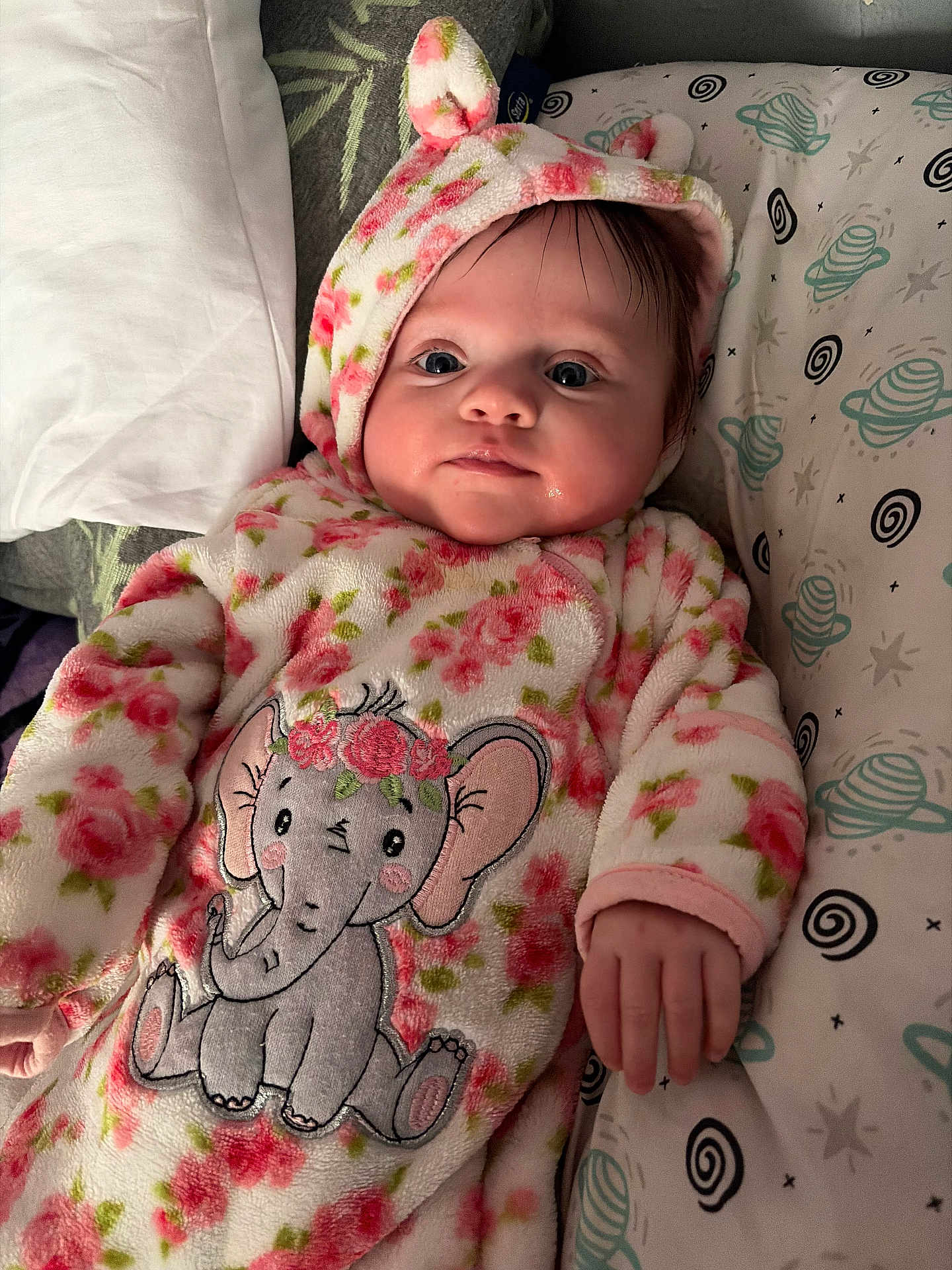 Nora is registered to the contest to win money with this photo: baby, infant, onesie, floral_pattern, elephant_design, pillow, bed, sleepwear, cute, child, portrait, indoor, cozy, soft_fabric, hand, face, head, expression, newborn, blanket