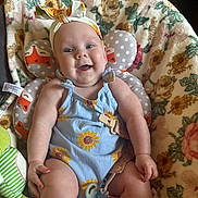 Berkley is registered to the contest to win money with this photo: baby, child, smiling, romper, headband, bow, flower_pattern, sunflower, cushion, fox_pattern, blanket, floral, sitting, indoors, cute, happy, infant, person, face, pacifier