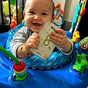 Lyam a rejoint le concours — aidez-le/la à gagner de superbes lots ! baby, infant, smiling, toy, activity_center, blue, hands, card, mouth_open, cheek, bracelet, plaything, seat, happy, portrait, close_up, indoor, crib, colorful, gaze