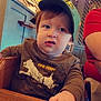 Brantley joined the competition — help win amazing prizes! toddler, child, cap, brown_shirt, high_chair, wooden_furniture, indoor, restaurant, curious_expression, person, hand, face, headwear, seated, table, lighting, lattice_wall, casual_clothing, young_child, baby