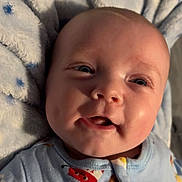 Jaxson is registered to the contest to win money with this photo: baby, infant, face, smile, blue_blanket, sleepwear, cute, cheeks, eyes, child, cozy, soft_texture, patterned_clothing, happy, portrait, closeup, skin, head, lying_down, indoors