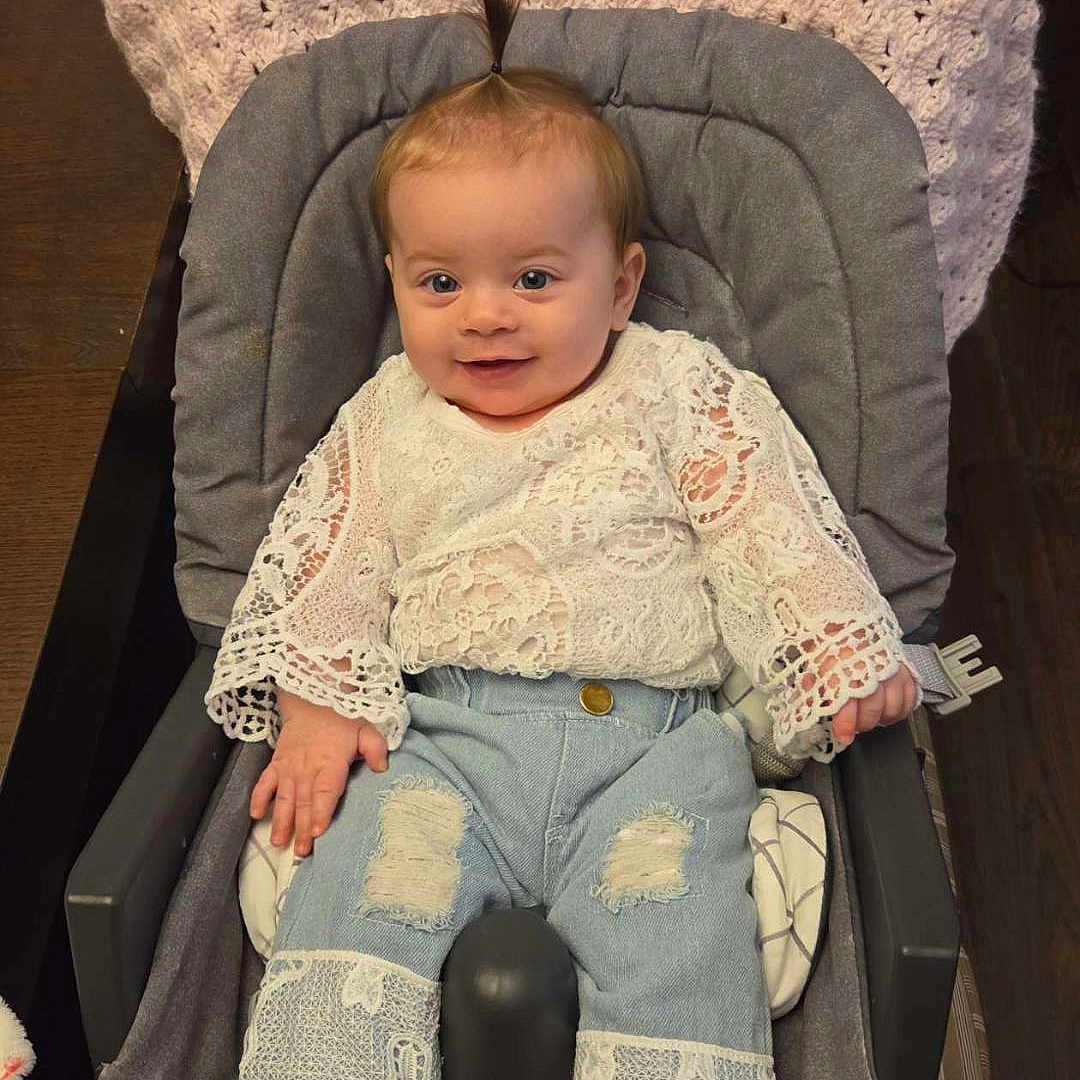 Gianna joined the competition — help win amazing prizes! baby, child, infant, smiling, lace_clothing, jeans, baby_seat, cushion, blanket, indoor, wooden_floor, happy, cute, portrait, person, young_child, small_hair_ponytail, sitting, comfortable, casual_clothing