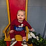baby, child, smiling, sitting, chair, red_chair, yellow_chair, maroon_clothing, sneakers, indoor, plants, potted_plants, white_flowers, gray_wall, portrait, cute, happy, person, throne, floor