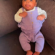 Kanyla is registered to the contest to win money with this photo: baby, infant, couch, purple_outfit, brown_couch, face, barefoot, indoors, person, child, sitting, cute, looking_up, handheld_device, relaxed, home, furniture, portrait, cozy, small_feet