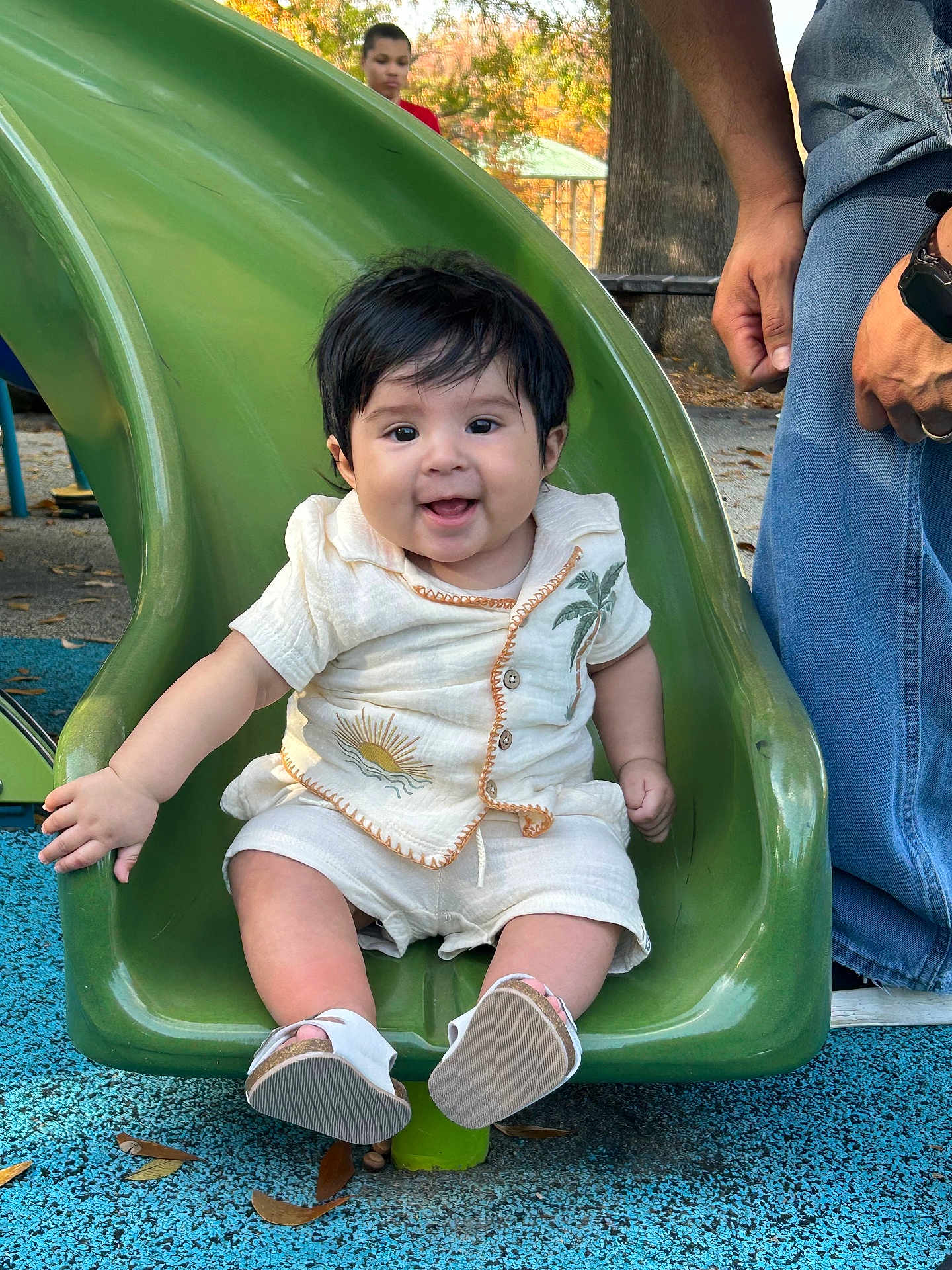 Luka joined the competition — help win amazing prizes! baby, child, slide, playground, green_slide, smiling, happy, outdoor, autumn, trees, person, jeans, hand, footwear, sun_embroidery, palm_tree_embroidery, casual_clothing, park, fall_leaves, fun