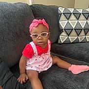 Ariyah joined the competition — help win amazing prizes! toddler, child, glasses, headband, pink, red_shirt, overalls, socks, couch, pillow, geometric_pattern, indoor, living_room, furniture, seated, cute, baby, portrait, person, casual
