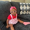 toddler, child, glasses, headband, pink, red_shirt, overalls, socks, couch, pillow, geometric_pattern, indoor, living_room, furniture, seated, cute, baby, portrait, person, casual